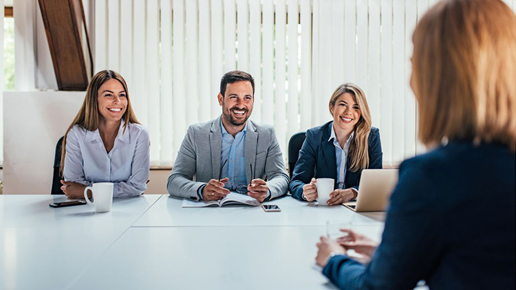 Bewerbungsgespräch mit einer Beewberin an einem großen Bürotisch und drei Persoonen gegenüber